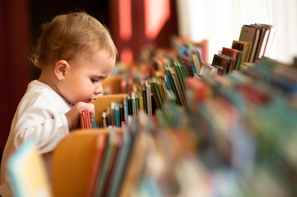 Un bébé fouille dans des bacs remplis de livre et d'albums colorés